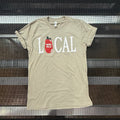 A beige graphic t-shirt with 'LOCAL' printed in white letters and a red tomato icon, laid flat on a black metal rack.